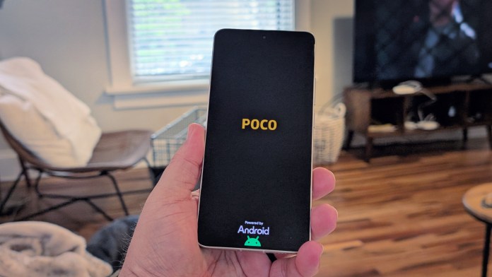 Людина, яка тримає смартфон PoCO, що відображає екран запуску з текстом 