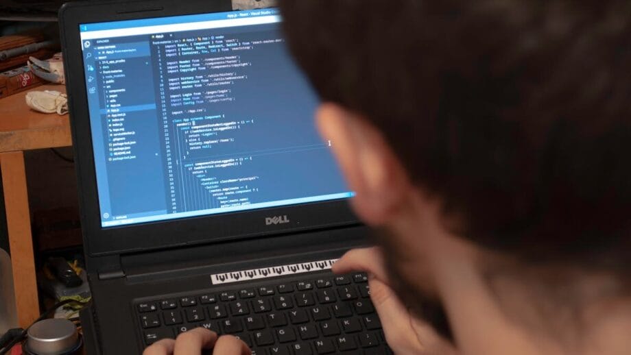 Особа, що вводить код на ноутбуці Dell у захаращеному робочому просторі. Екран відображає інтерфейс програмування.