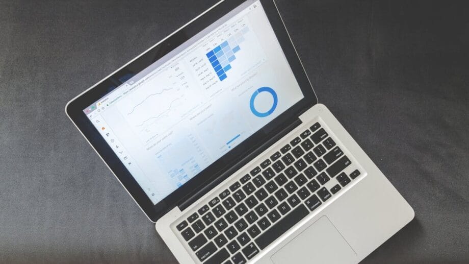 Відкритий ноутбук із діаграмами даних і графіками на екрані на темній поверхні, де видно дерев’яну підлогу.